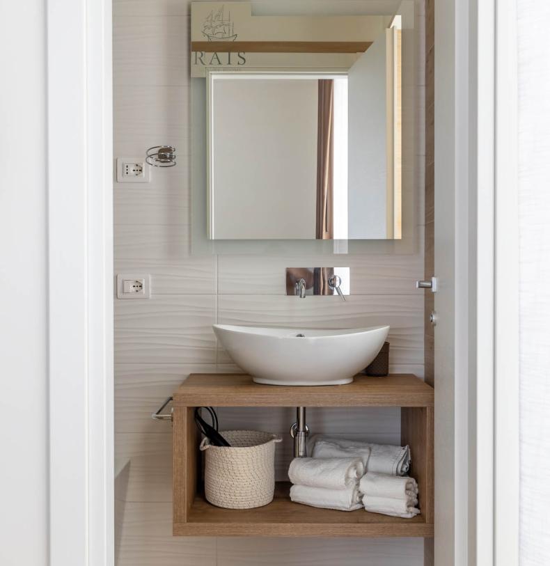 Bagno moderno con lavabo bianco e scaffale in legno.